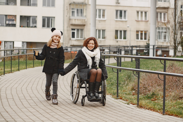 disabled woman in wheelchair with daughter. family walking outside at park